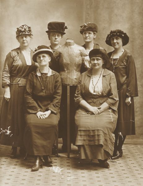 Posed group of six women with a dressmaker's dummy.
