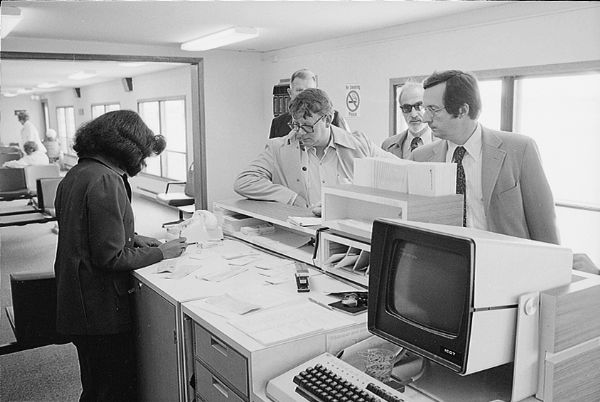 Congressman David R. Obey (right) at the check-in counter at a Wisconsin airport. This view from behind the counter shows a woman checking his ticket and the technology in use.