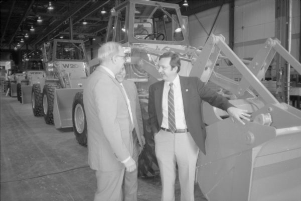 Congressmen Les Aspin and David R. Obey of Wisconsin at the J.I. Case plant. The group is standing near a line of farm equipment manufactured by the company.
