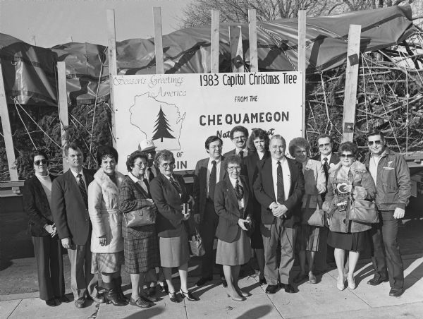 Congressman David R. Obey (standing below the C) greets a delegation from Wisconsin that accompanied the official Capitol Christmas Tree cut in the Chequamegon National Forest. They are posed in front of the semi-trailer holding the Christmas tree.