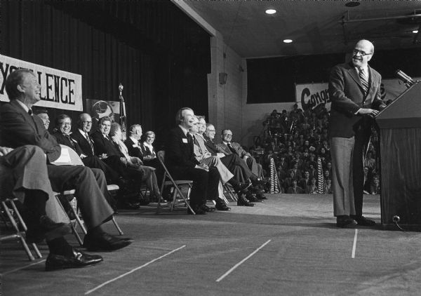 During his remarks, Senator Gaylord Nelson, who is standing at the podium, cracks a joke, apparently at the President's expense. Wisconsin dignitaries to the left of President Jimmy Carter who could be identified (all Democrats) are Governor Martin Schreiber, State Senator William A. Bablitch of Stevens Point, State Senator Fred Risser, Congressman Alvin Baldus, Secretary of DNR Anthony Earl, former Governor Patrick J. Lucey, and Congressman Henry Reuss.