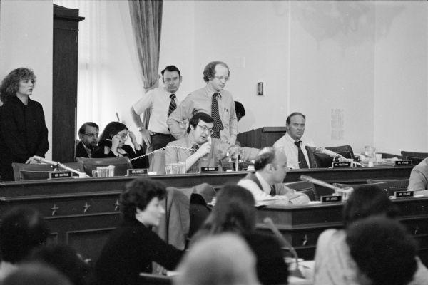 Congressman David R. Obey talks on the telephone during a break in the deliberation of the House Budget Committee. Standing above Obey is his aide Scott Lilly.
