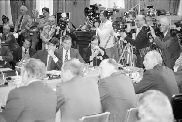 Arms control talks between visiting Soviets and American legislators. Wisconsin Congressman David R. Obey sat in on the talks with Congressman Tom Downey, who headed the panel. Both men are listening to a translation with chins in hand. Photographers are in the background.