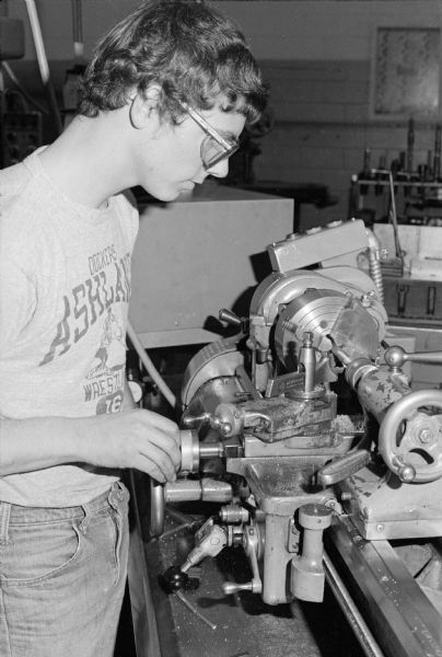 A student using an engine lathe in an auto mechanics class at Indianhead Technical Institute. He is wearing safety glasses, jeans and an Ashland wrestling t-shirt.