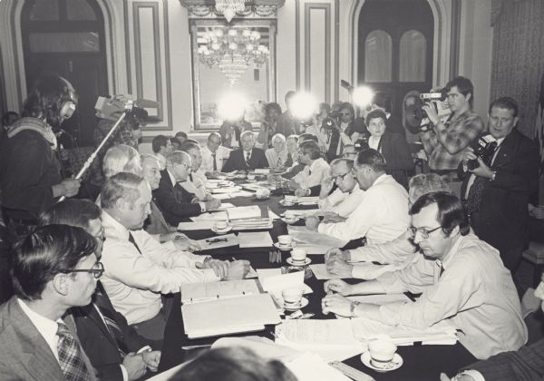 An emergency budget cutting session, under the watchful eye of the press. Wisconsin Congressman David R. Obey is at the far right of the table. Opposite him is Stuart Eisenstad, President Jimmy Carter's domestic policy adviser, Jim Free Cater's budget director: and Senator Jim Culver of Iowa. At the end of the table are Speaker Jim Wright and Senators Robert Byrd and Alan Cranston. The table is covered with notebooks, papers and many cups of coffee.