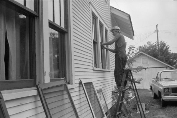 During a tour of his district Wisconsin Congressman David R. Obey visited various sites where energy-saving projects were underway. Here a workman on a ladder is improving the energy efficiency of a residence, probably replacing caulk around the windows.