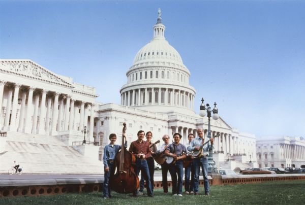 Photograph taken to illustrate the jacket of a recording issued by the Capital Offenses, the blue grass band headed by Congressman David R. Obey of Wisconsin (second from the left), who played the harmonica.  Others in the band included his sons Douglas (on Obey's right), and Craig (on Obey's left), as well as Scott Lilly, a member of his congressional staff. The United States Capitol building is behind them. A bicyclist is riding near the steps on the left.