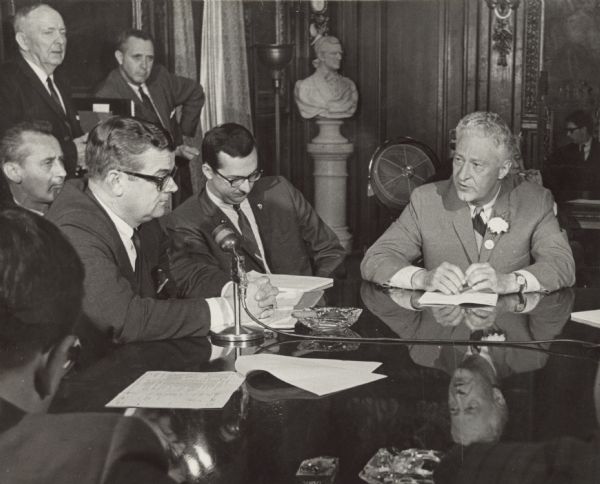 Republican Governor Warren P. Knowles meeting with the Democratic leadership: left to right Robert T. Huber, minority leader, and David R. Obey, assistant minority leader. Also identified are State Senator Jerris Leonard (back to camera), in the background is State Representative Ray Tobias (sitting), and standing (from left to right) State Senator Frank Panzer, and Paul Hassett, aid to the governor. The meeting was in the governor's conference room and the topic of discussion was the state budget.