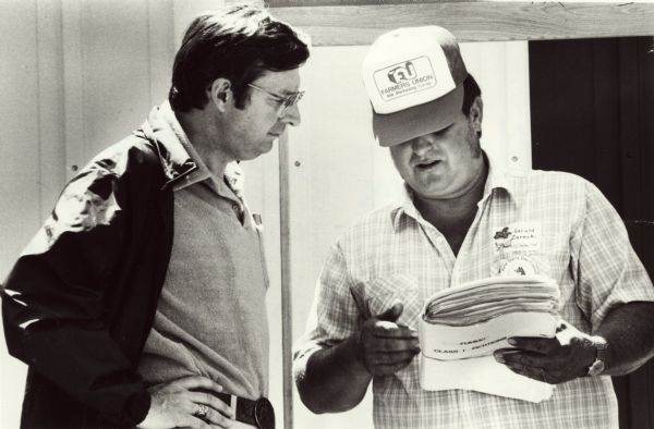 Jerry Zarecki (in the hat), president of the Portage County Farmers Union, presents Wisconsin Congressman David R. Obey with one folder of petitions collected by the Wisconsin farmers protesting the discriminatory dairy pricing provisions of the 1985 Farm Bill. The folder was part of over 10,000 mid-western names that Obey was to take back to Washington. The petitions were presented as part of that county's June Dairy Day.