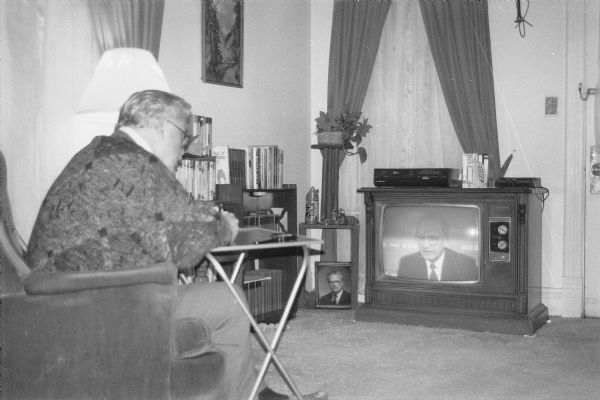 Man watching a program on a large television. In front of him is a TV tray. There is a VCR on top of the television. Although unidentified it is likely that it was taken in Stevens Point in April 1991.