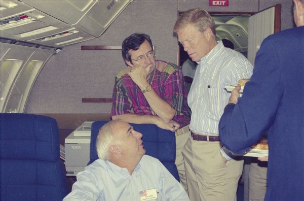 Speaker of the House Dick Gephardt (standing right) during a flight back to Washington after a House leadership tour of the Persian Gulf. With Gephardt are two Wisconsin congressmen who were also on the tour, Les Aspin (seated) and David R. Obey.