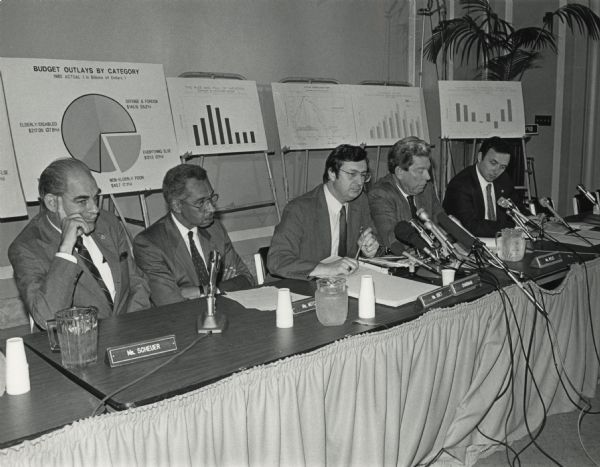 Under the chairmanship of David R. Obey of Wisconsin (center) the congressional Joint Economic Committee held hearings in Wisconsin. In the background are numerous charts used to convey economic information to the audience.