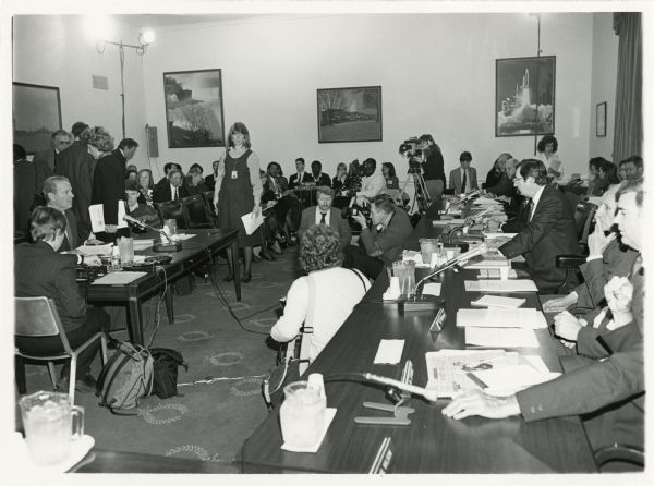 Secretary of State James Baker testifying before the Foreign Operations Subcommittee of the House Appropriations Committee. Wisconsin Congressman David R. Obey, opposite Baker and leaning forward, chaired the subcommittee. Other names written on back of photo, Matt McHugh, Terry Peele and John Porter.