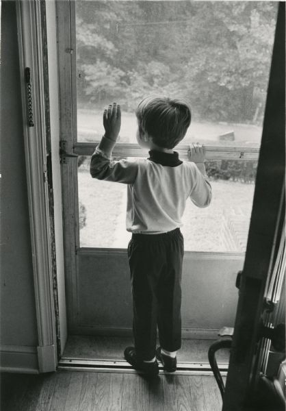 Craig, son of David Obey, seen from the back, waves out the window of a screen door.