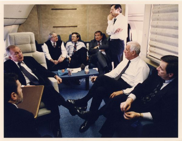 Congressman David Obey on a diplomatic airplane with a group of seated colleagues. He is standing on the right.