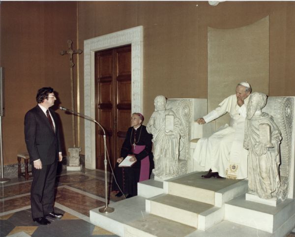 Congressman David Obey meets Pope John Paul II. Obey stands at the microphone while Pope John Paul II is seated on his throne.