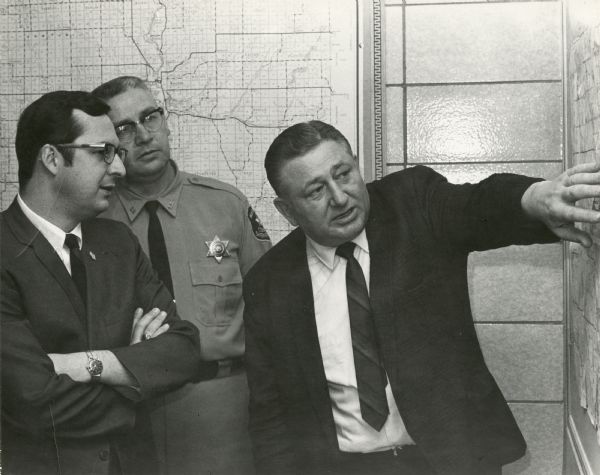 State Assemblyman David Obey, Marathon County Sheriff Louis Gianali and Harvey Woodward looking at a map. Harvey Woodward was a veteran of law enforcement service in Marathon and Lincoln counties for 35 years.