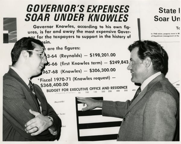 State Representatives David Obey and Joe Sweda facing each other at a press conference. The sign behind them reads, "Governor's Expenses Soar Under Knowles." Below is the explanation for calling Governor Knowles "the most expensive Governor for the taxpayers to support in the history of Wisconsin."