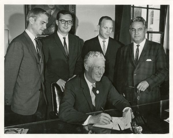 Governor Warren Knowles (seated) signing the Technical Education Re-Organization Bill or the Higher Education Reorganization Bill, a.k.a. the Obey-Nikolay Bill. Standing, left to right: Assemblymen William Steiger, David Obey, Frank Nikolay and Paul Alfonsi.

