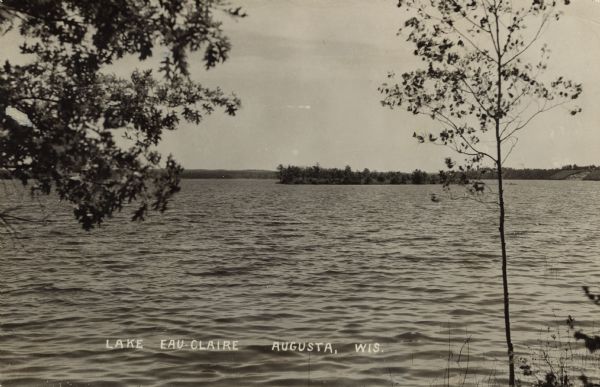 Photographic postcard view from shoreline of Lake Eau Claire and a small island. Caption reads: "Lake Eau Claire, Augusta, Wis."