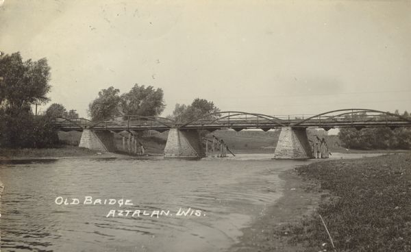 Photographic postcard view from shoreline of an old bridge over the Rock River. Caption reads: "Old Bridge, Aztalan, Wis."