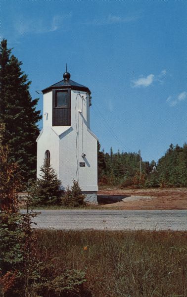 Color postcard of a small, tower-like building on the side of a road.