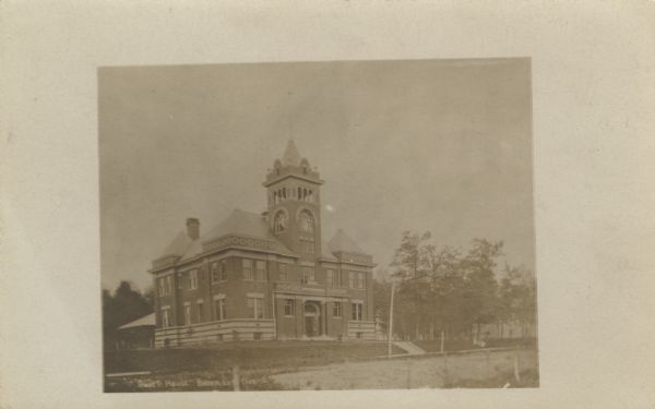 Photographic postcard view of the exterior of the Court House. A large belfry is above the arched entrance way.
