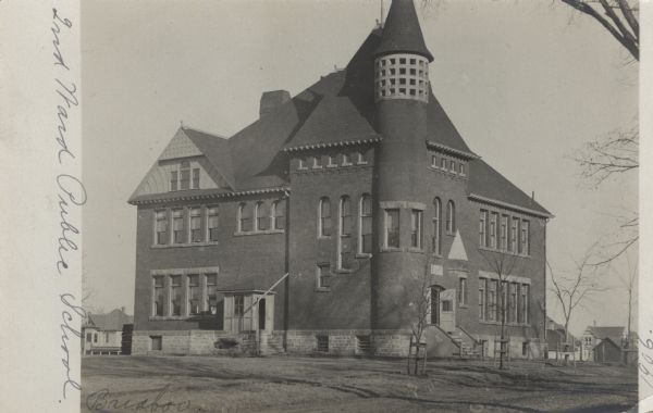 Photographic postcard view of the exterior of the public school, a large brick building with a turret in the corner.