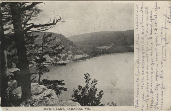 View from bluff of Devil's Lake. A road runs along the far shoreline. Caption reads: "Devil's Lake, Baraboo, Wis."