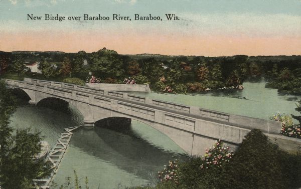 Colorized postcard of an elevated view of a concrete bridge over a river. There is a boat near wooden pilings that stretch from the shoreline to the center of the bridge. Trees and flowering shrubs line both banks. There are farms on the far side of the river. Caption reads: "New Birdge [sic] over Baraboo River, Baraboo, Wis."