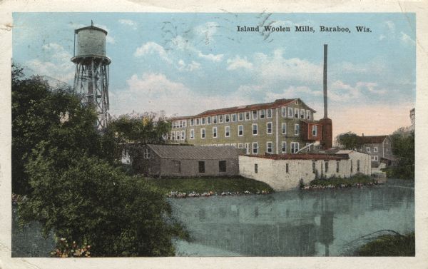 Colorized postcard view of the exterior of the woolen mill along the banks of a river. A water tower is on the left, and a smokestack is on the right. Caption reads: "Island Woolen Mills, Baraboo, Wis."