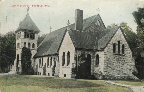 Colored postcard of the exterior of the stone church. There are four crosses, one on the bell tower, and three others at the corners of the roof. Windows and entrances are arched, and vines grow along some of the sides of the stone walls. Caption reads: "Trinity Church, Baraboo, Wis."