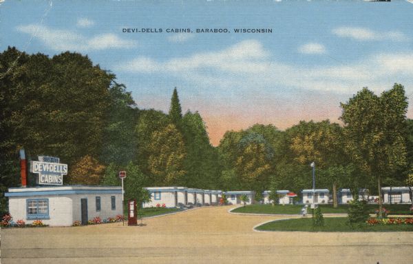 Colorized postcard view of the exterior view of a motel. A neon sign over the main building. A gas pump is in the drive. Caption reads: "Devi-Dells Cabins, Baraboo, Wis."