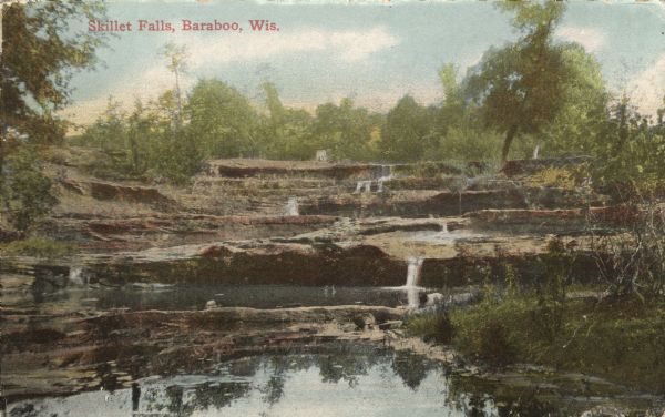 Colorized postcard view of Skillet Falls from downstream. Caption reads: "Skillet Falls, Baraboo, Wis."
