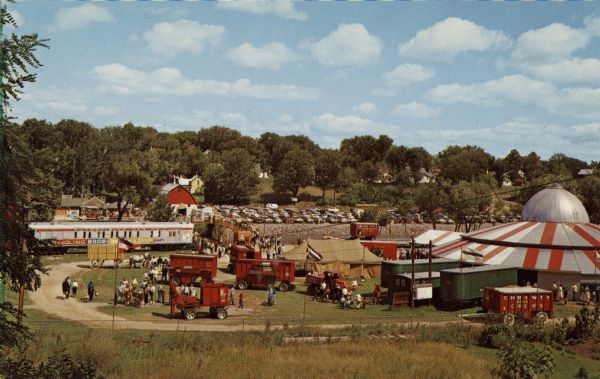 Elevated view of the Circus World complex, with railroad cars, a tent and the arena where the circus shows are held. There is a parking lot in the background.