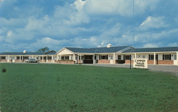 View across lawn towards the exterior of a motel. A station wagon parked in front of one of the units.