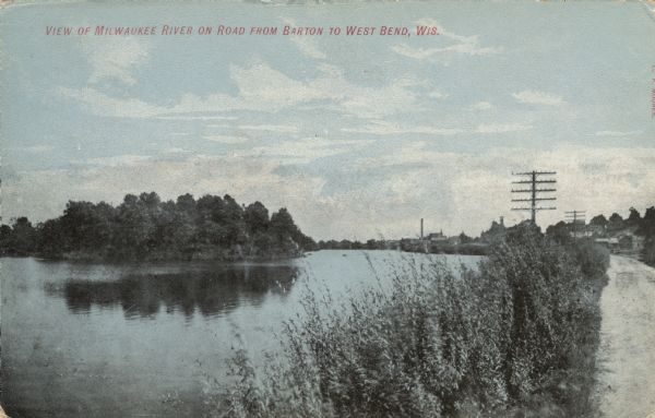 Colorized postcard view of the Milwaukee River from the road. There are buildings in the background on the right. Caption reads: "View of Milwaukee River on Road from Barton to West Bend, Wis."
