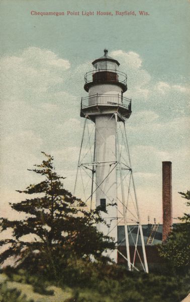 Colorized postcard view of a lighthouse, with a building and a smokestack behind it. Caption reads: "Chequamegon Point Light House, Bayfield, Wis."