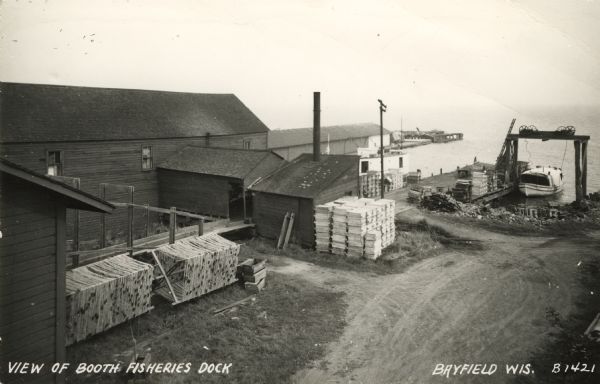 Photographic postcard of an elevated view of the fishery and its dock. Caption reads: "View of Booth Fisheries Dock."