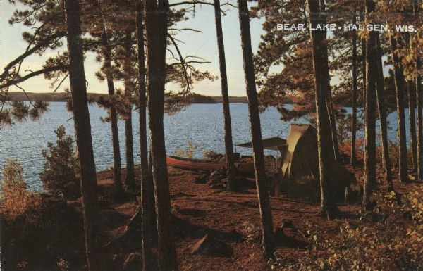 Elevated view of a tent and canoe in the woods by a lake.