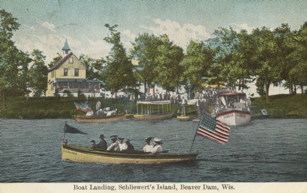Colorized postcard view over water towards boats and boaters at a resort. In the background are people and boats near a pier. The resort is among trees on the far shoreline. Caption reads: "Boat Landing, Schliewert's Island, Beaver Dam, Wis."