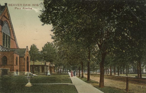 Colorized postcard view down the sidewalk of a tree-lined street in a residential neighborhood. Pedestrians are on the sidewalk in the front of what may be a church building on the left. Caption reads: "Beaver Dam, Wis. Park Avenue."