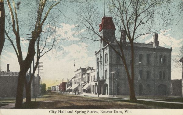 Colorized postcard view down the unpaved street, with the city hall building on the corner on the right. Caption reads: "City Hall and Spring Street, Beaver Dam, Wis."