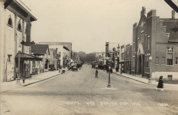 Photographic postcard view down a city street lined with commercial buildings and automobiles. Caption reads: "White Way, Beaver Dam, Wis."