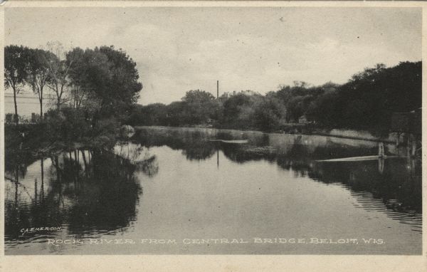 Photographic postcard view of the Rock River with trees along the banks. There is a smokestack in the distance. Caption reads: "Rock River from Central Bridge, Beloit, Wis."