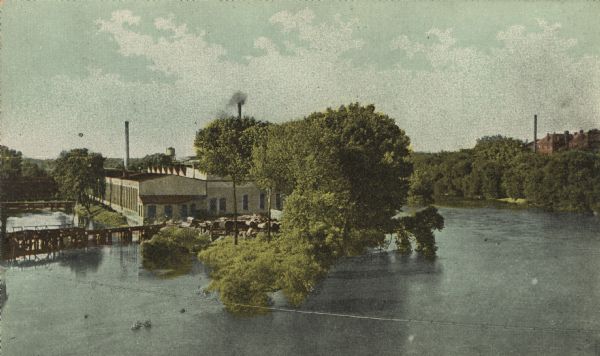 Colorized postcard view of the iron works and river. There is another factory on the opposite side of the river behind the trees on the right.