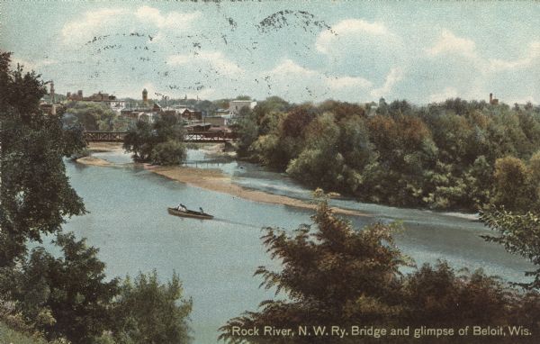 Colorized postcard of an elevated view through trees of the Rock River, with a railroad bridge and a glimpse of Beloit. There are boaters near sandbars in the river. Caption reads: "Rock River, N.W. Ry. Bridge and glimpse of Beloit, Wis."