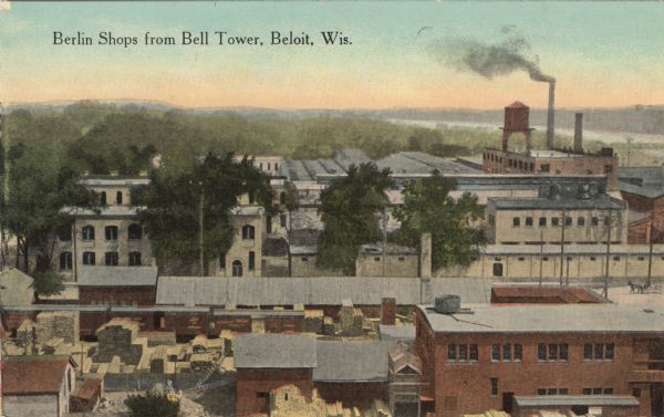 Colorized postcard of an elevated view of Berlin Shops. There are piles of lumber and freight cars in the foreground. A factory with a water tower is in the background. In the far distance is the Rock River. Caption reads: "Berlin Shops from Bell Tower, Beloit, Wis."