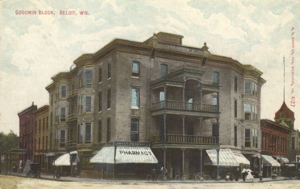 Colorized postcard view from the street of the Goodwin block, featuring a hotel and a pharmacy. Several bicycles are parked at the curb. Caption reads: "Goodwin Block, Beloit, Wis."