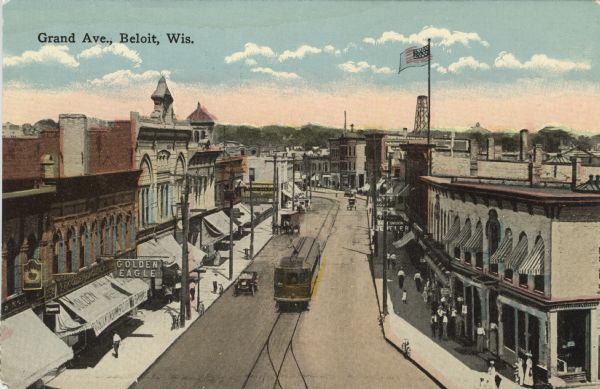 Elevated, colorized postcard view of a street in a central business district. Streetcar tracks run down the center of the street, and automobiles are driving along the curbs. Caption reads: "Grand Ave., Beloit, Wis."